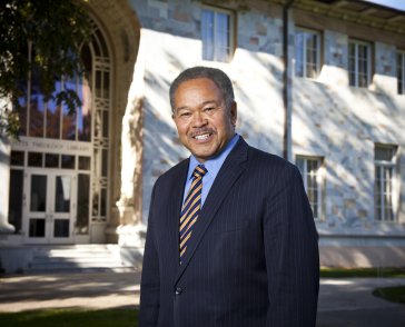 Headshot of a man in a navy blue suit in front of a white building